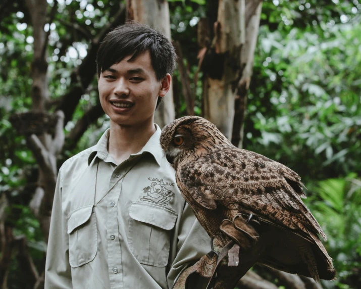 a man holding an owl while standing in the woods