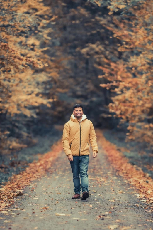 a man in a brown jacket standing on the road in front of yellow trees