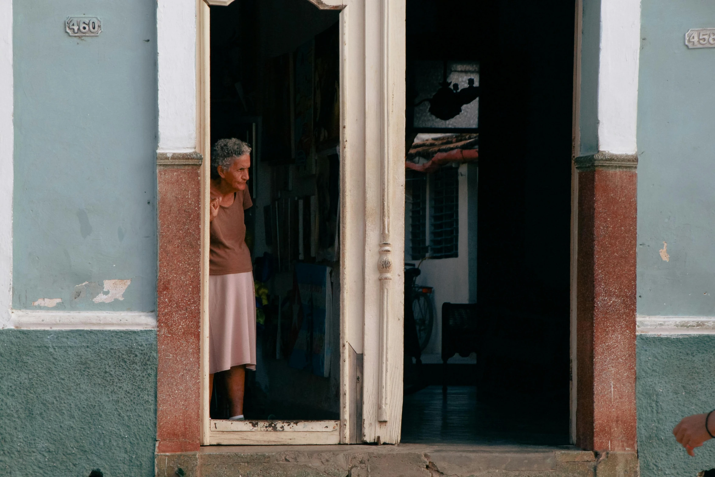 woman peering through open doorway at dog looking in