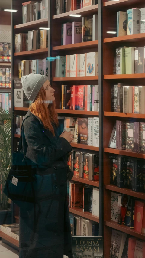 a woman leaning against a book shelf reading a novel