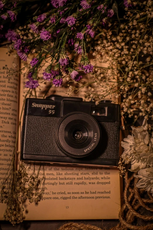 a book is sitting next to a camera and flowers