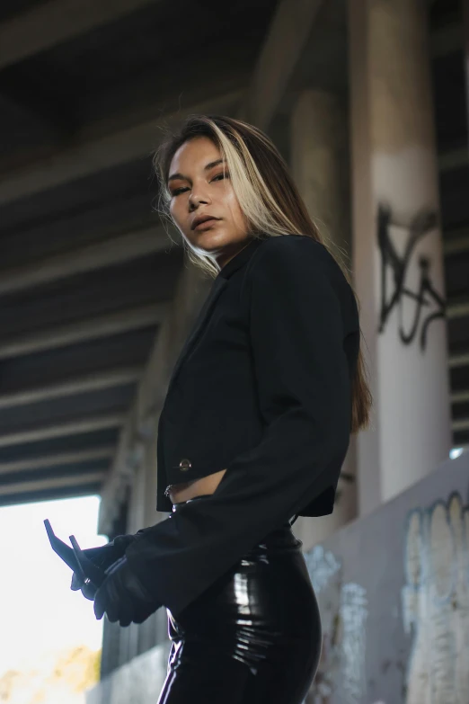 a woman in black leather pants standing under an overpass