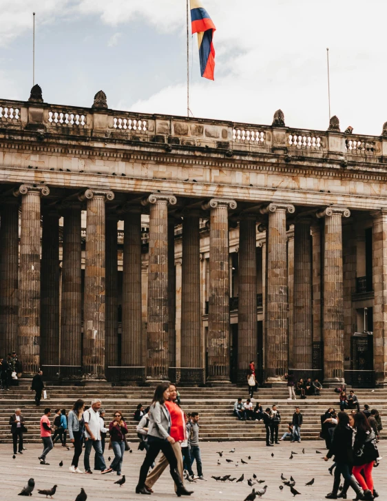 people walking around in front of a building with a lot of birds