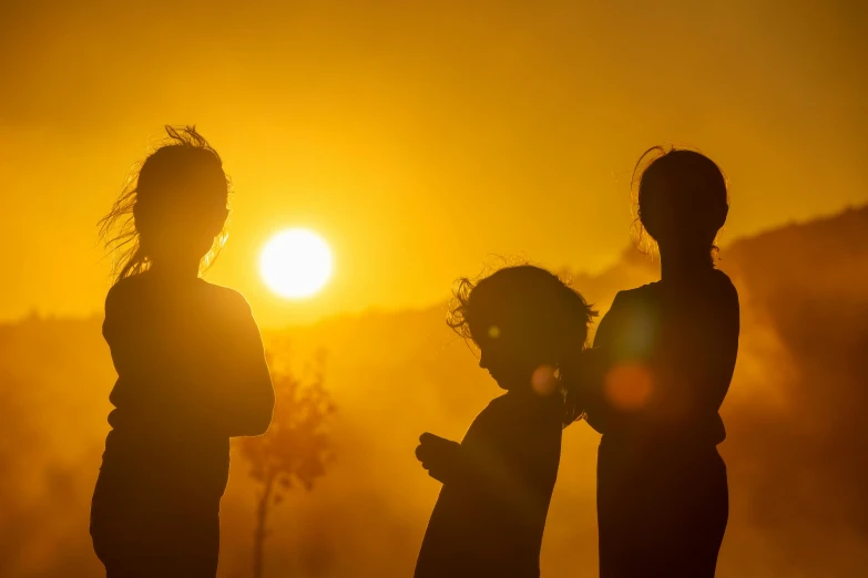 three children standing in silhouette at sunset