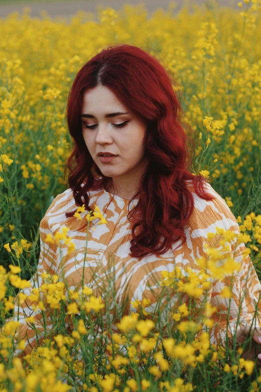 a woman with red hair stands in a field full of yellow flowers