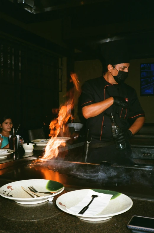 a man standing at a counter with plates on it and a fire burning in the center