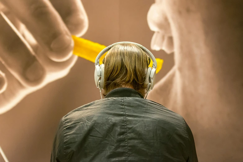 man in headphones and jacket facing a computer screen with hand with yellow marker on it