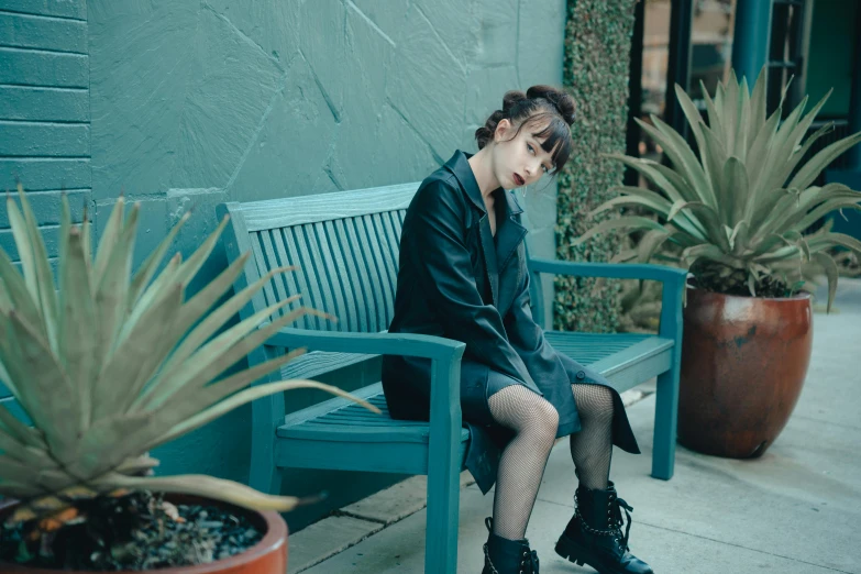 a girl is sitting on a bench next to some plants