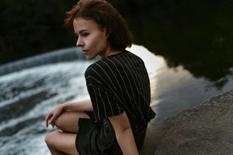 a girl sitting by the water and looks at soing