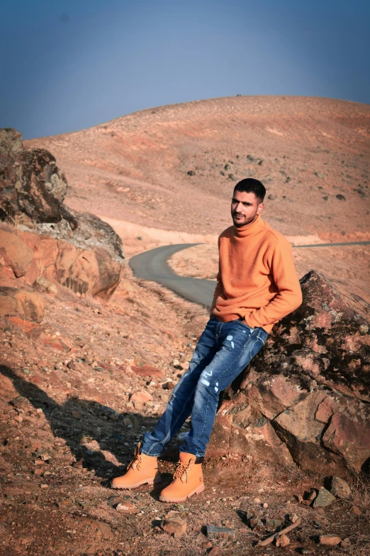 man sitting on rock with orange sweater on