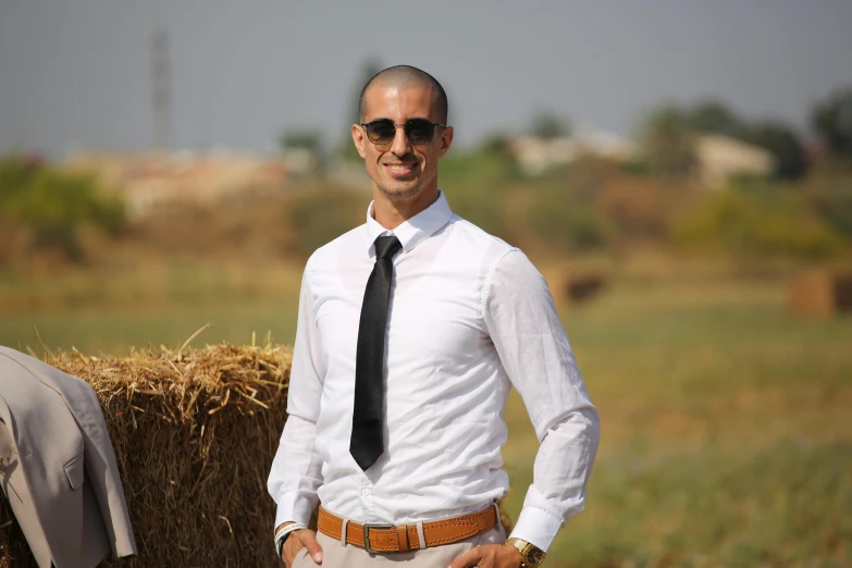 a man in sunglasses and a tie standing next to a bale of hay
