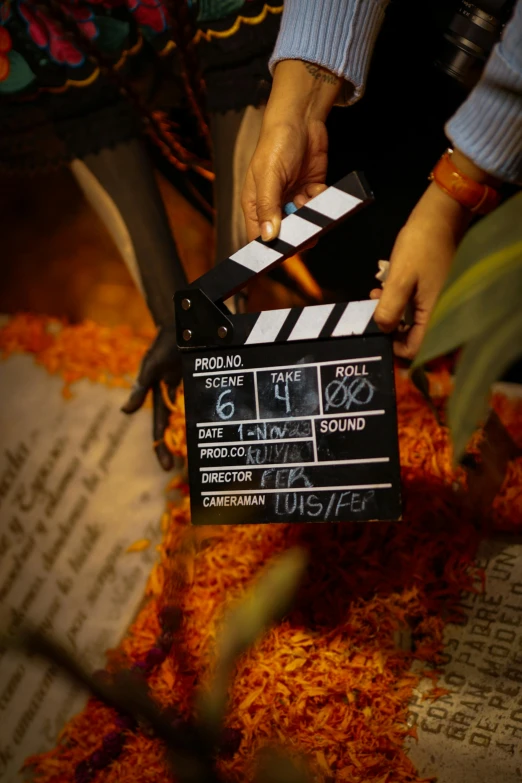 person holding up a black and white clapper with writing on it