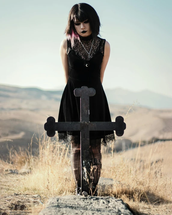 a woman with long hair and black dress stands next to a cross