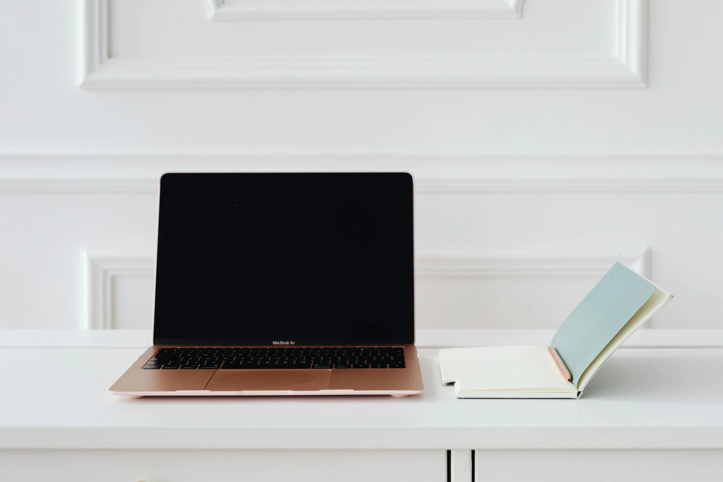 a laptop is on a white surface and a notepad is next to it