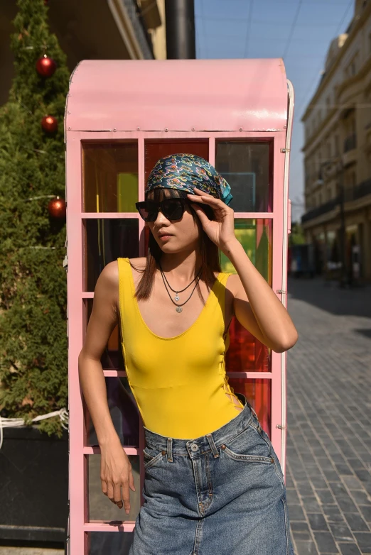 a woman in sunglasses and a hat standing in a pink phone booth