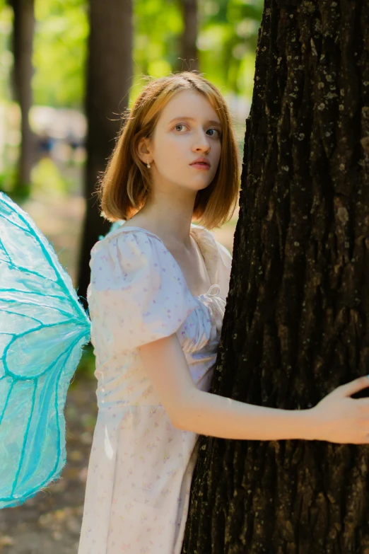 a woman in white dress holding a blue erfly wing next to a tree