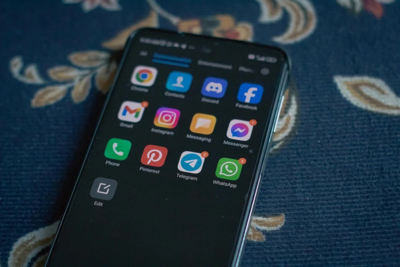 an iphone with several icons on the screen sitting on a blue floraled blanket