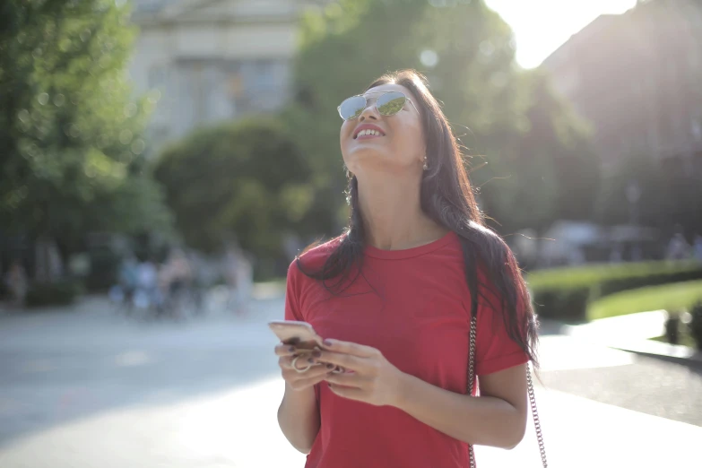 young woman in red shirt looking up at her cell phone