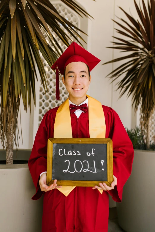 a young man in red graduation clothes holding a class graduation sign