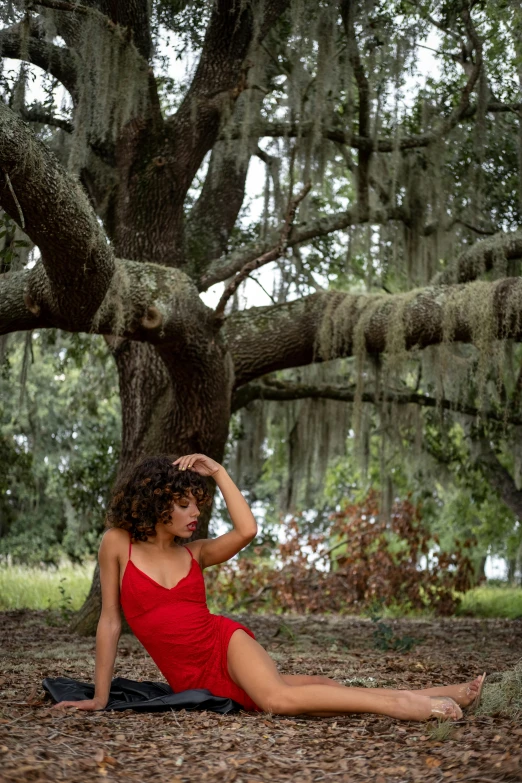 a woman is sitting on the ground in front of a tree