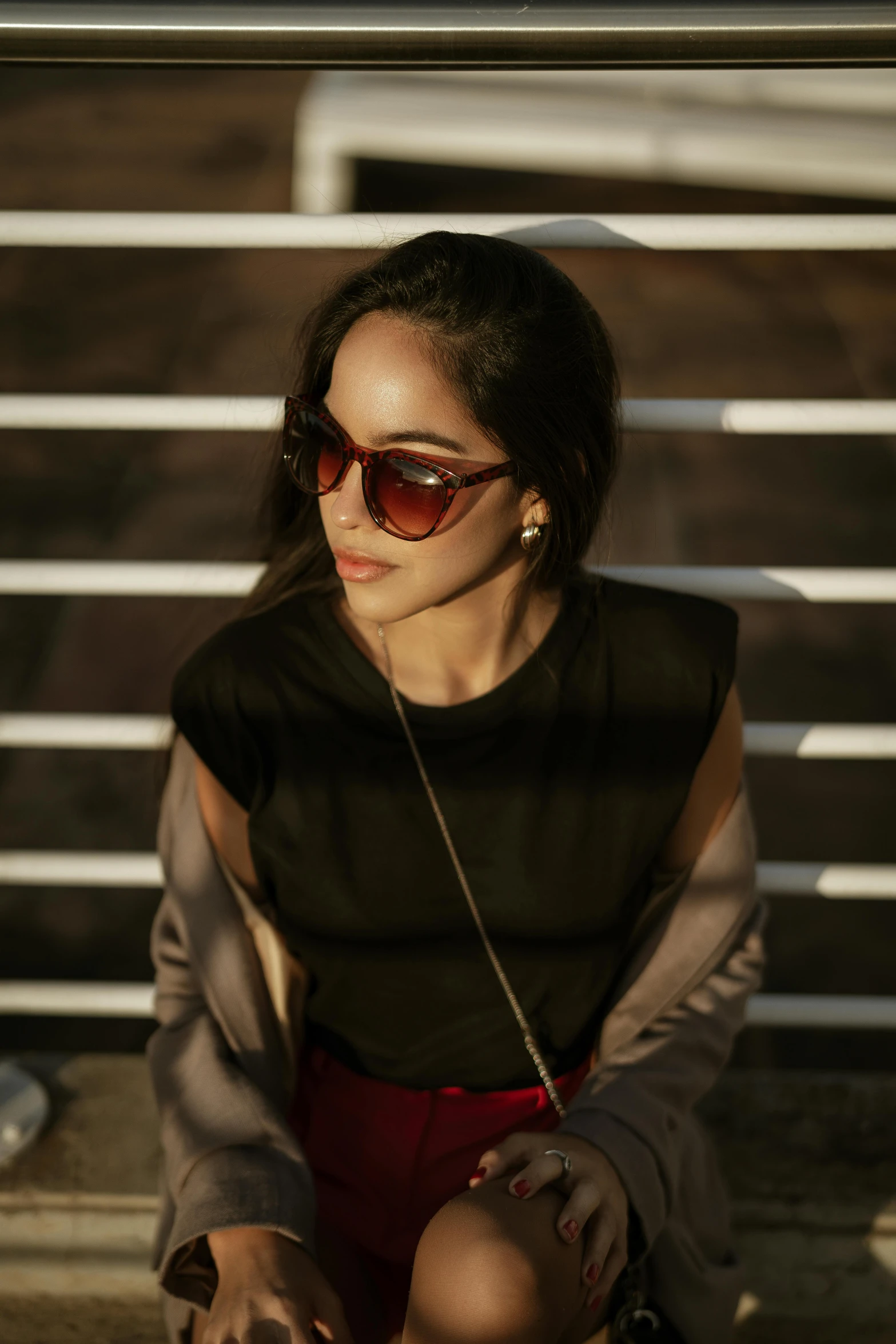 a woman sitting down wearing red pants and sunglasses