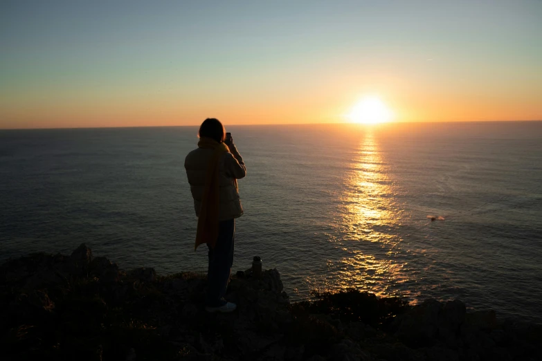 person on cliff overlooking ocean during sunset in natural setting