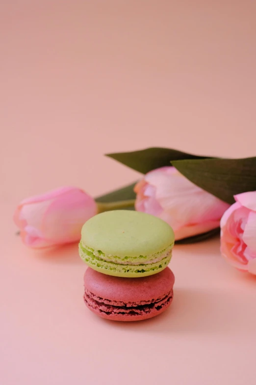 pink roses and green and yellow macaroons sitting in front of them