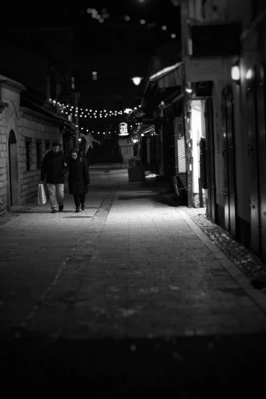 two people walk along a dark alley way at night