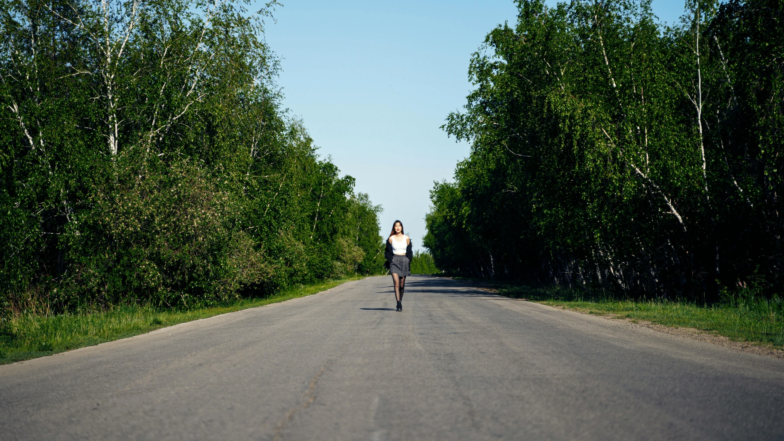 person standing on long skateboard on empty road with trees