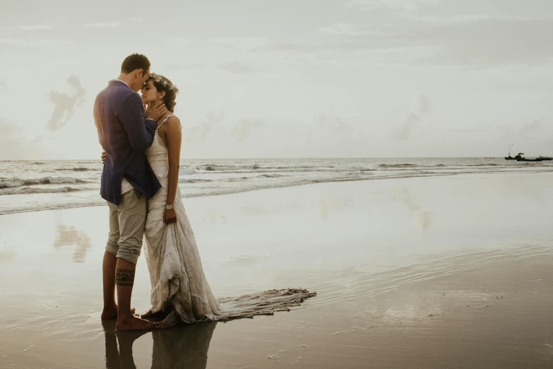 a bride and groom kissing in front of the water on the beach