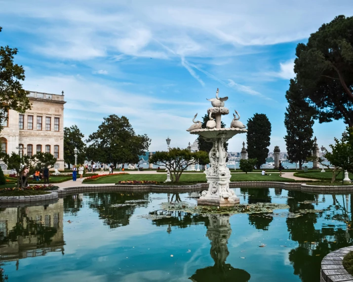 a pond has several fountains and trees in the background