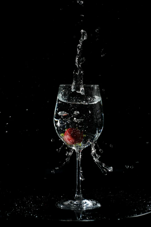 a red strawberry being dropped into an empty wine glass