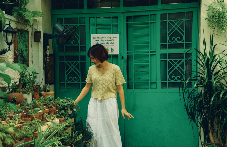 a woman walking into a green door with many potted plants