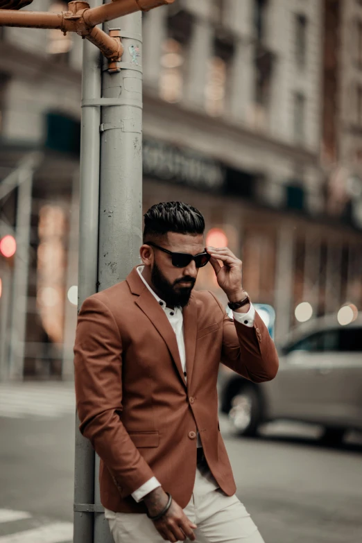 the man is posing by the street pole wearing his suit and sunglasses