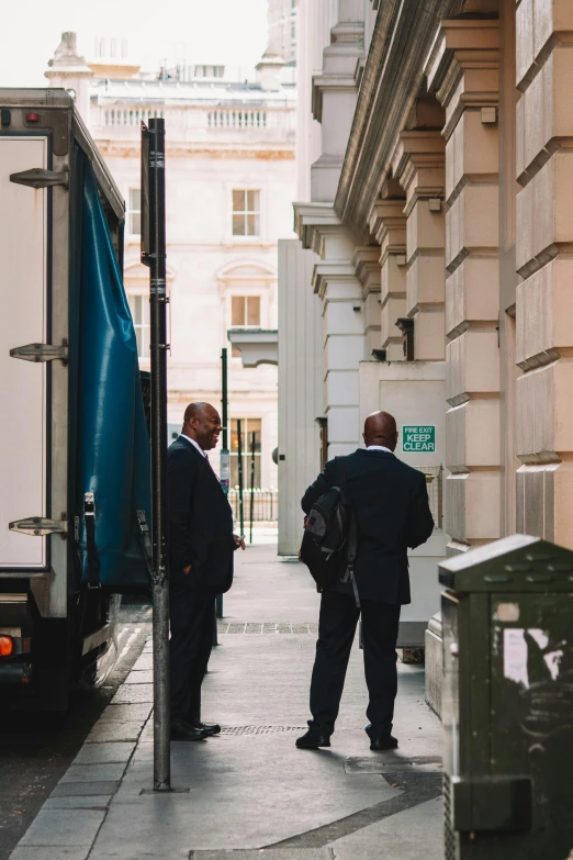 two men stand on a sidewalk next to an entrance