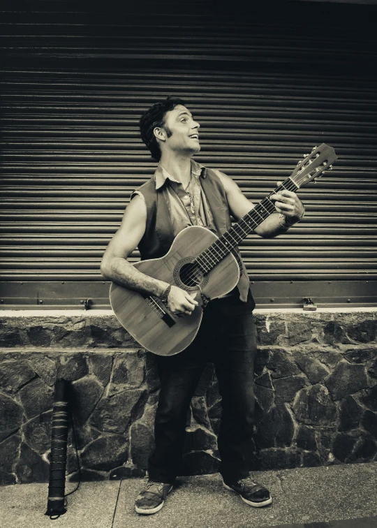 a man holding an acoustic guitar standing on a sidewalk