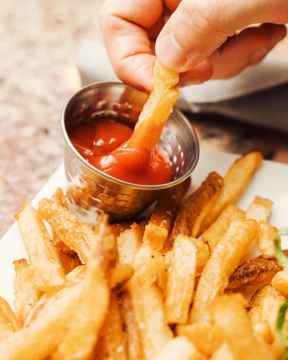 someone dipping a  dog into fries with ketchup on the side