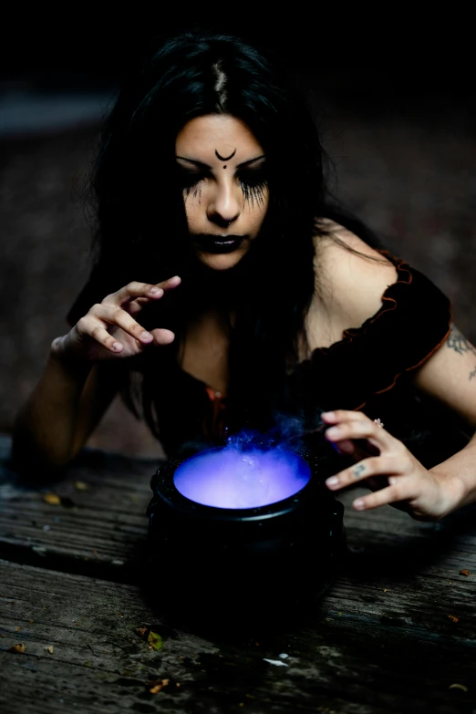 a woman wearing a witch makeup holding a glowing blue bowl