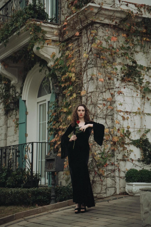 a woman in black dress standing on brick walkway with ivy