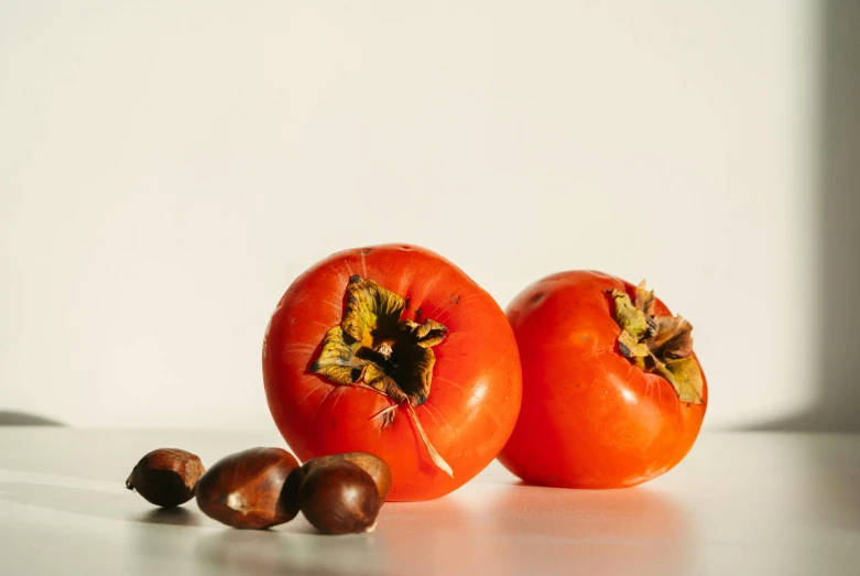 two tomatoes and some walnuts sitting on a white table