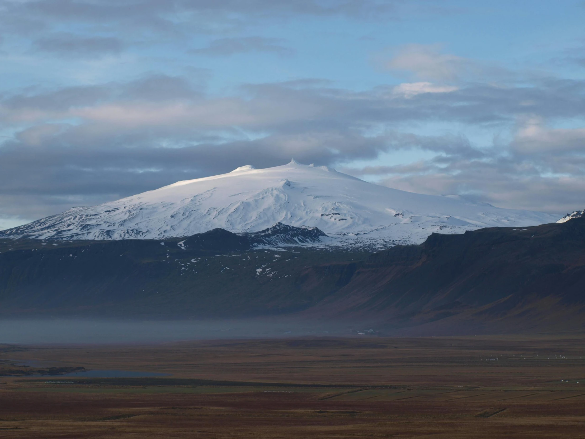 a snowy mountain on the horizon with fog and clouds