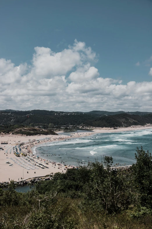 view from a hill looking down at a beach and a long line of boats