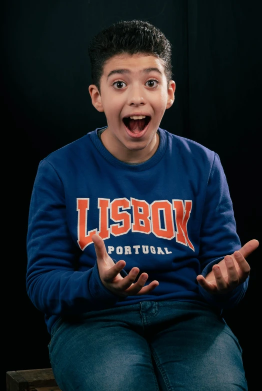 a boy holding his hands out while sitting in front of a black background