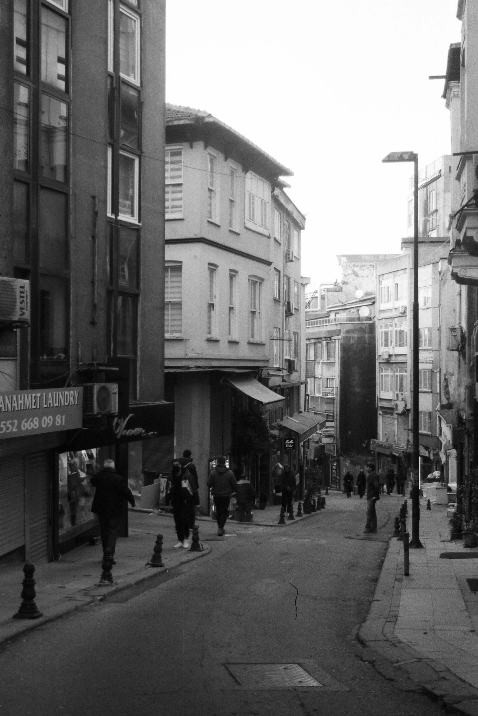 people walk down the narrow street near many tall buildings