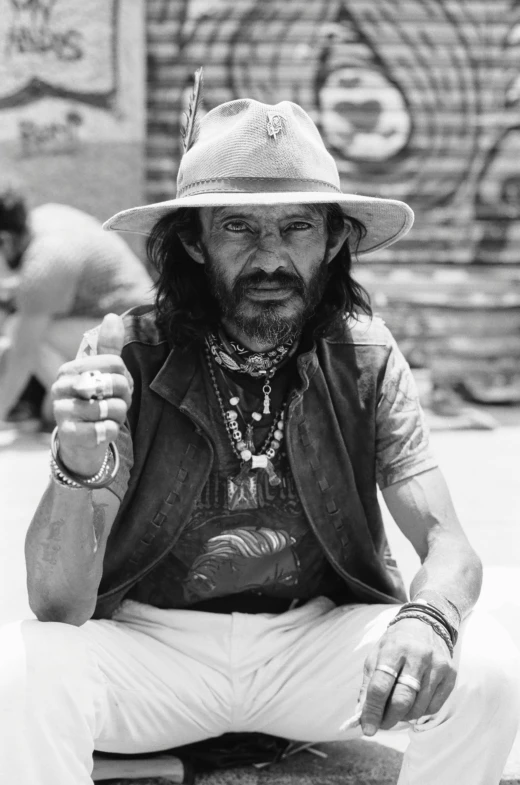 a man wearing a hat smoking a cigarette and sitting down