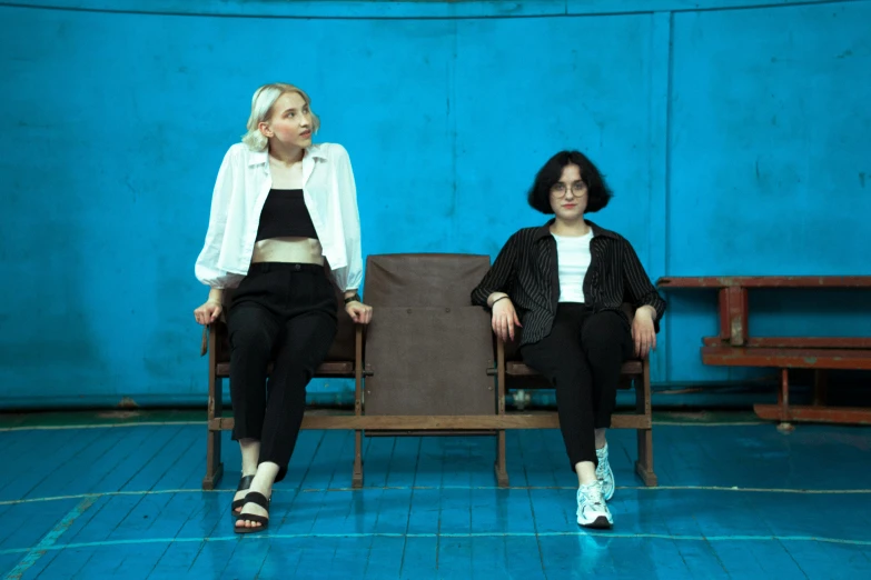 two women sitting on wooden chairs in a blue room