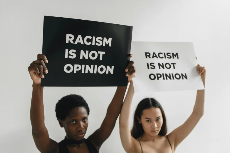 two women holding signs, with one standing and the other holding the same sign