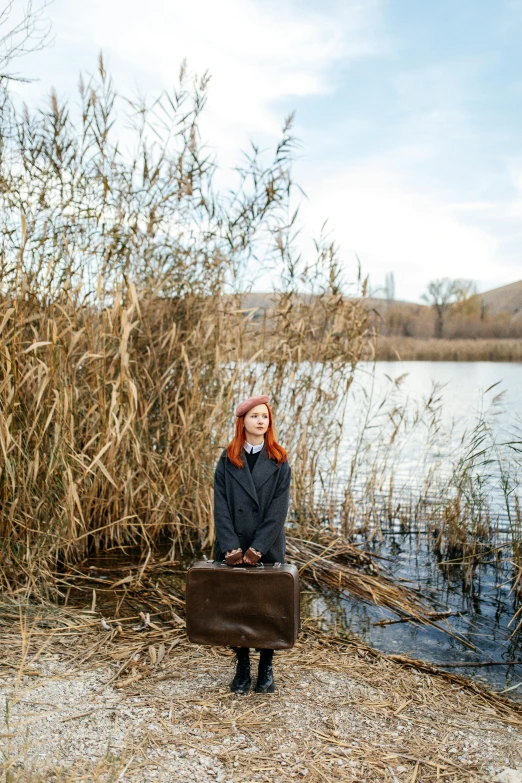 woman in black coat posing with briefcase by water