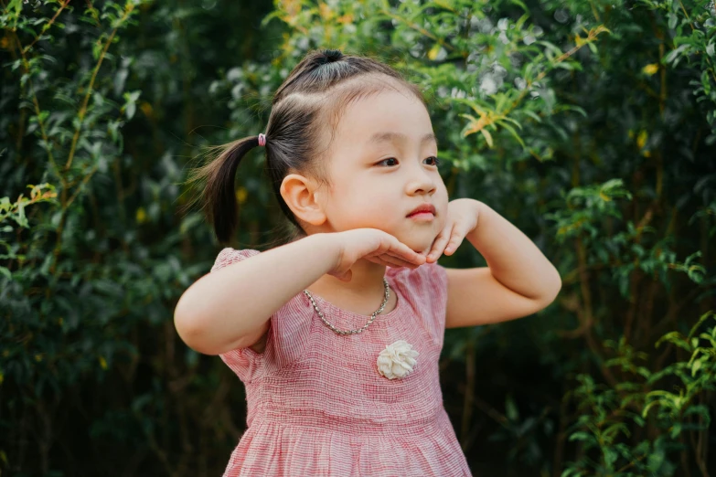 a little girl wearing pink clothing poses near some bushes