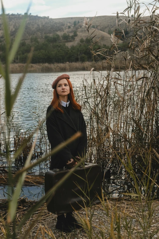 a woman with red hair is sitting on a bench next to a lake